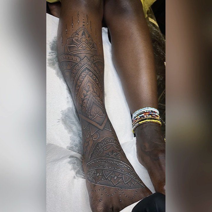Intricate dark brown henna patterns on a person's dark skin leg and foot.