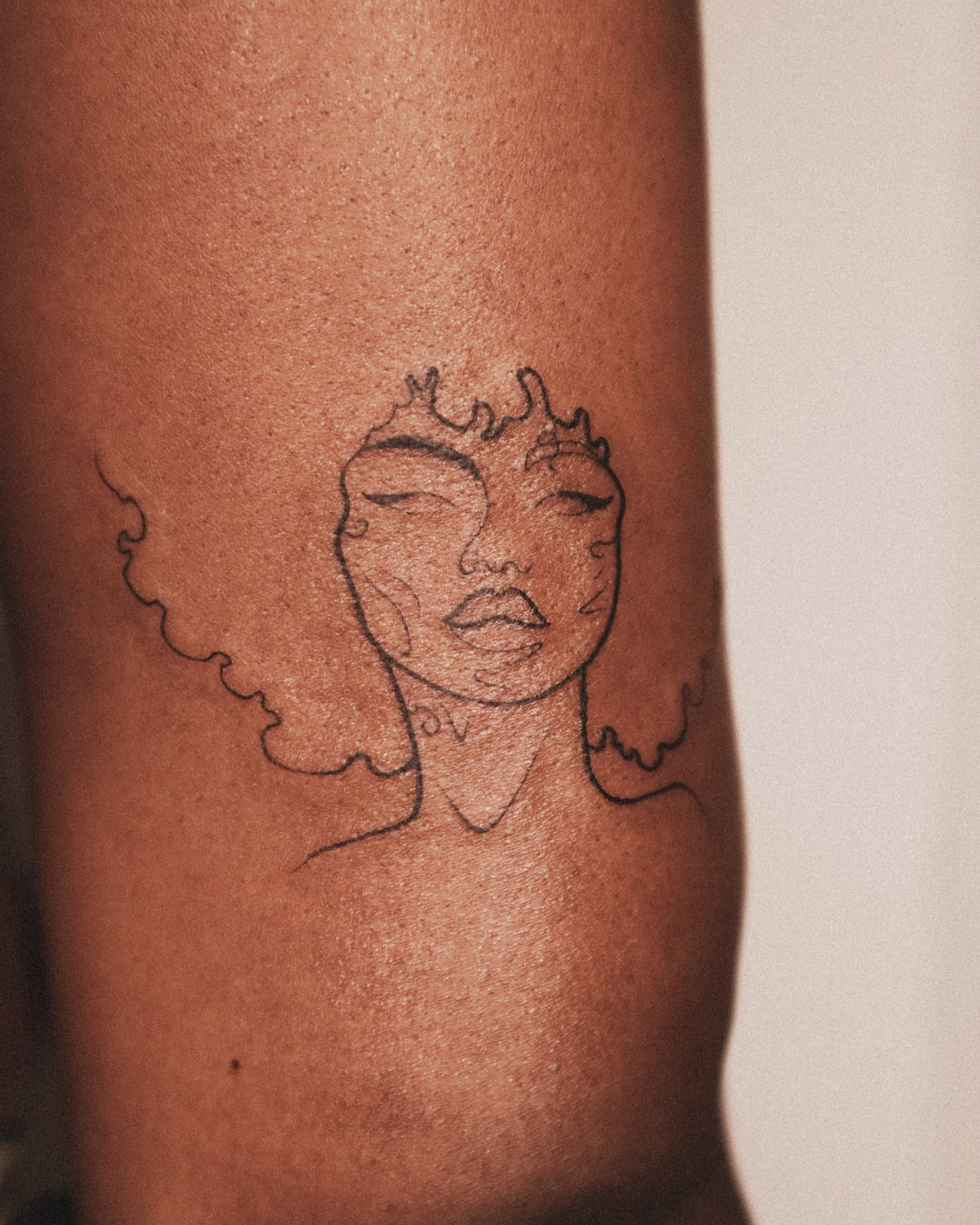 Minimalist fine-line tattoo of a woman's face on dark brown skin.