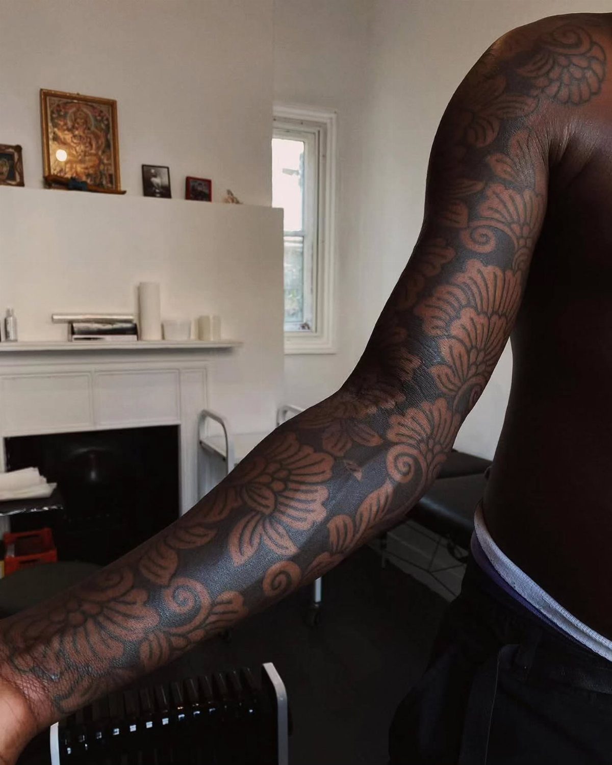 Dark skinned arm with a detailed floral and swirl sleeve tattoo.