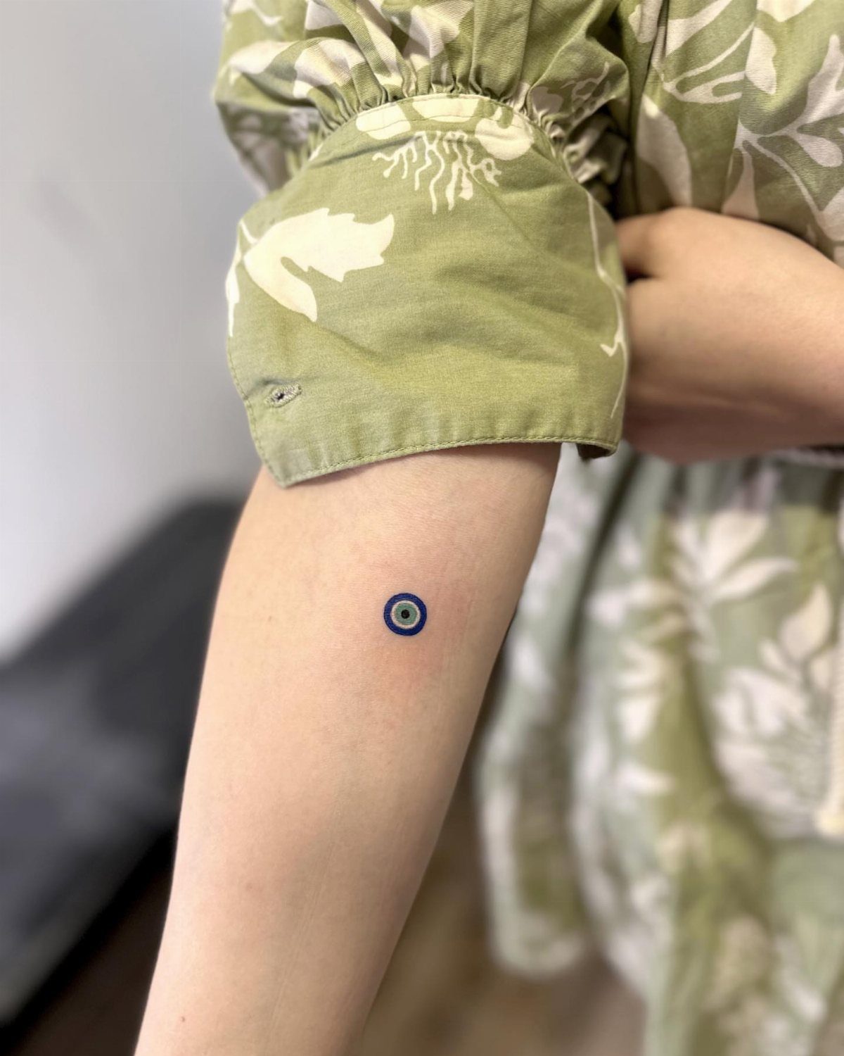 Small blue and black evil eye tattoo on a person's upper arm