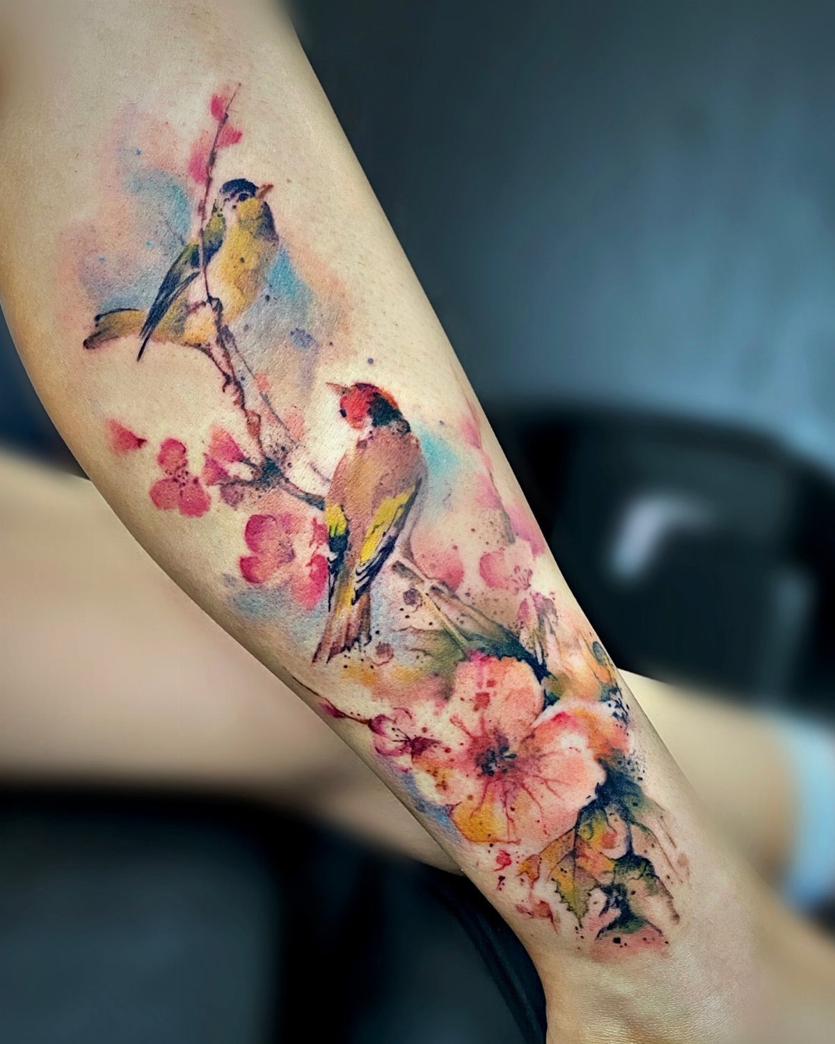 Watercolor tattoo of two birds on a flowering branch on a person's arm