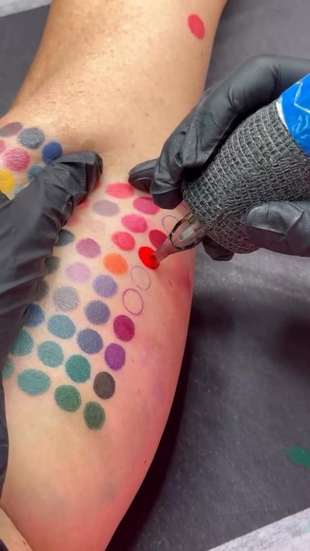 Tattoo artist applying a red ink dot to a colorful grid on an arm.