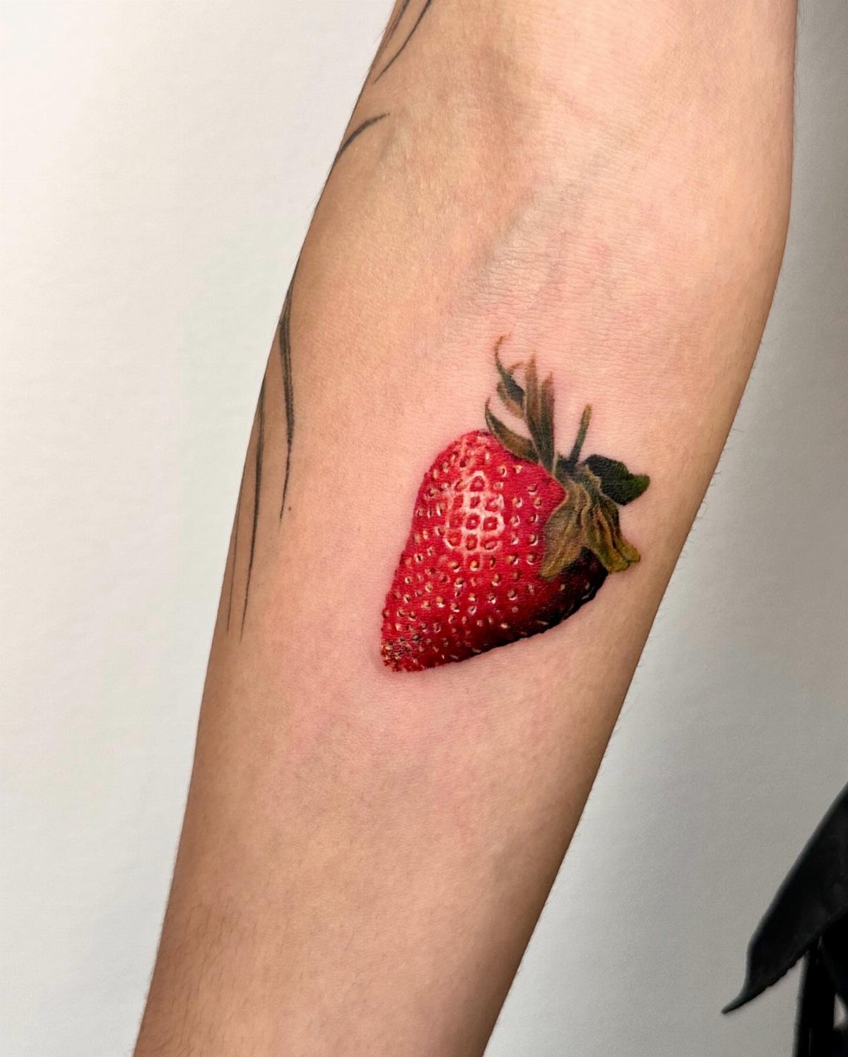 Realistic red strawberry tattoo with green leaves on a person's forearm