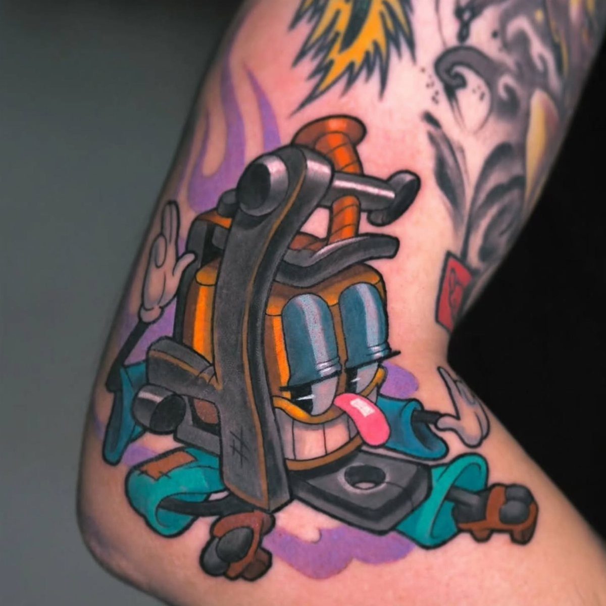 Cartoon tattoo machine with a face and tongue surrounded by colorful flames.