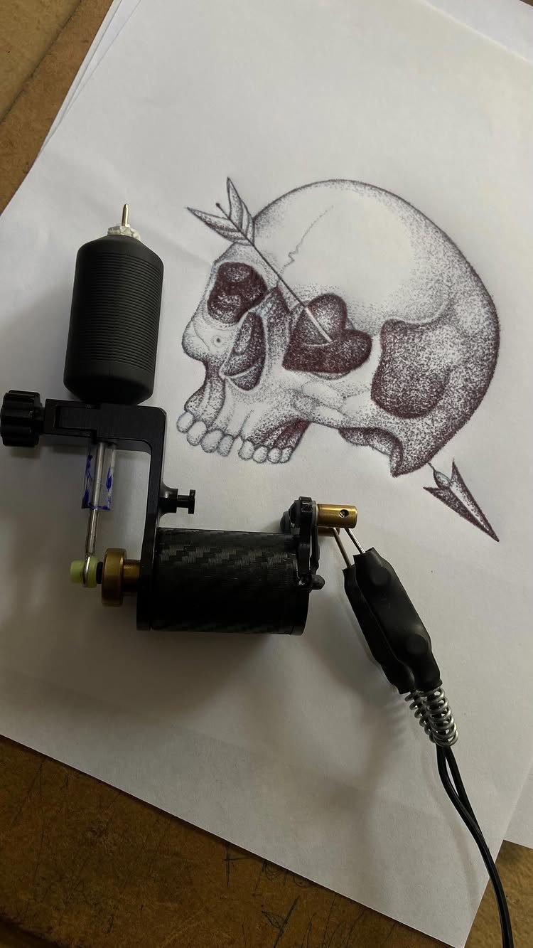 Tattoo machine resting on a drawing of a skull pierced by an arrow
