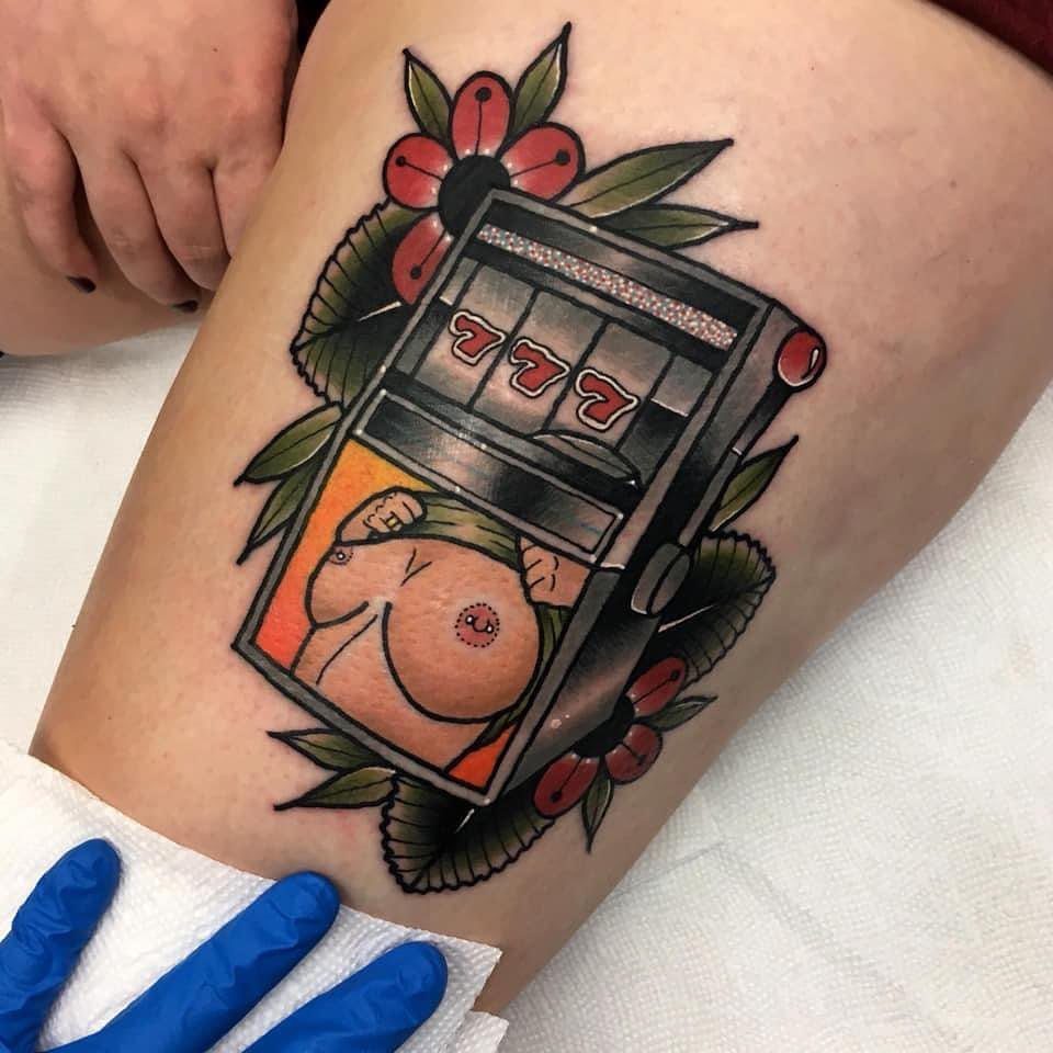 Slot machine tattoo with lucky 777 and red flowers on a thigh.