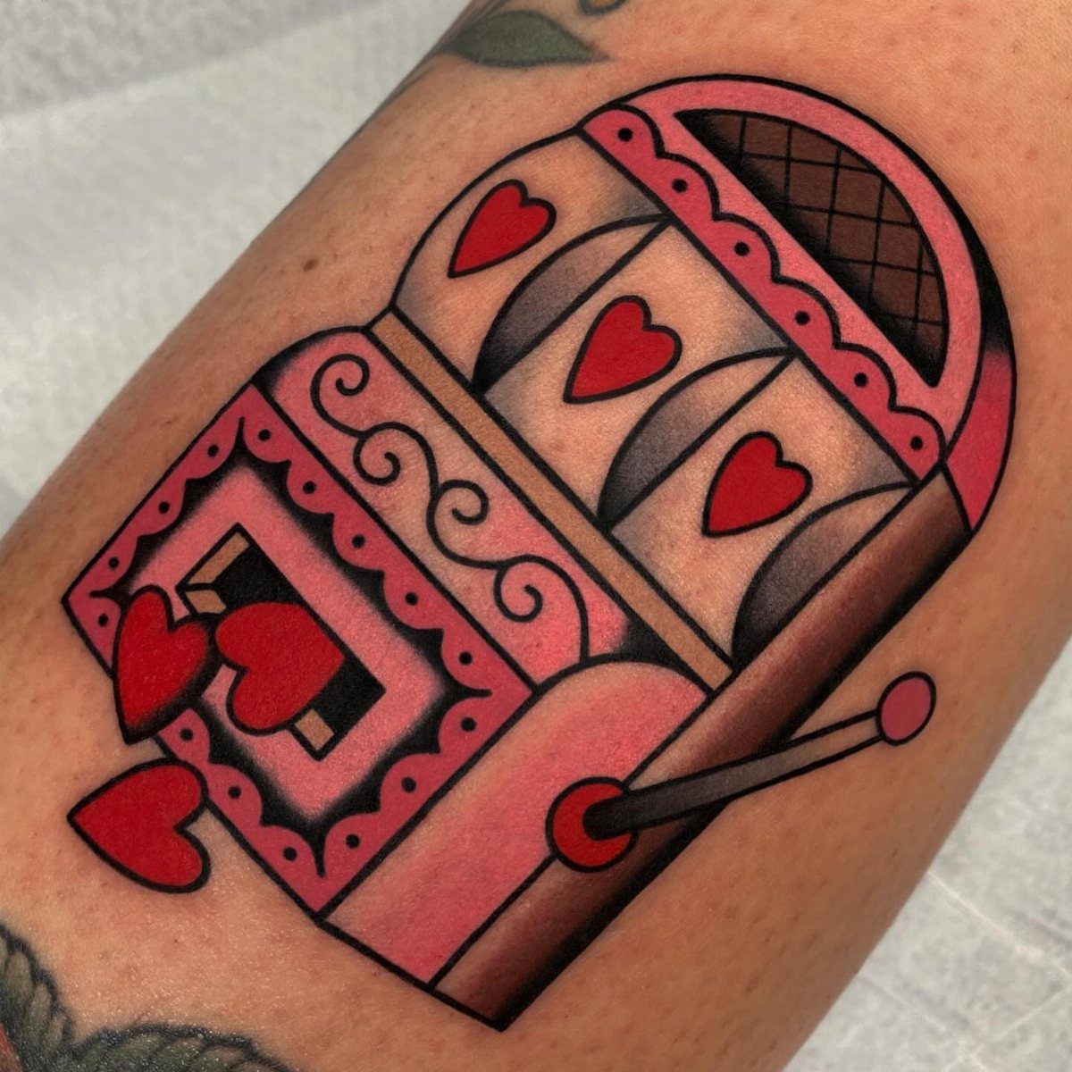 Pink slot machine tattoo with red hearts on a person's skin.