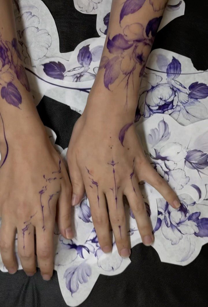 Purple floral tattoo stencils applied to arms and hands resting on patterned paper.