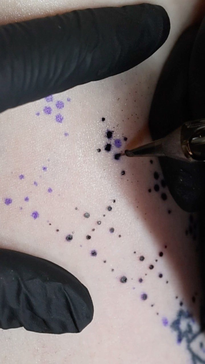 Tattoo machine applying ink to a purple geometric stencil on a person's arm.