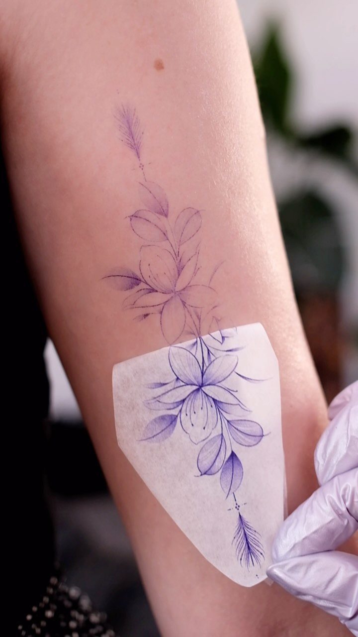 Floral tattoo stencil being peeled off a person's arm to reveal purple design.
