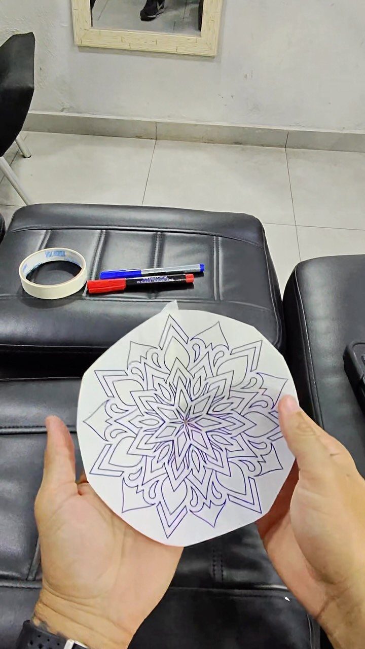 Hands holding a purple mandala tattoo stencil outline on white paper.