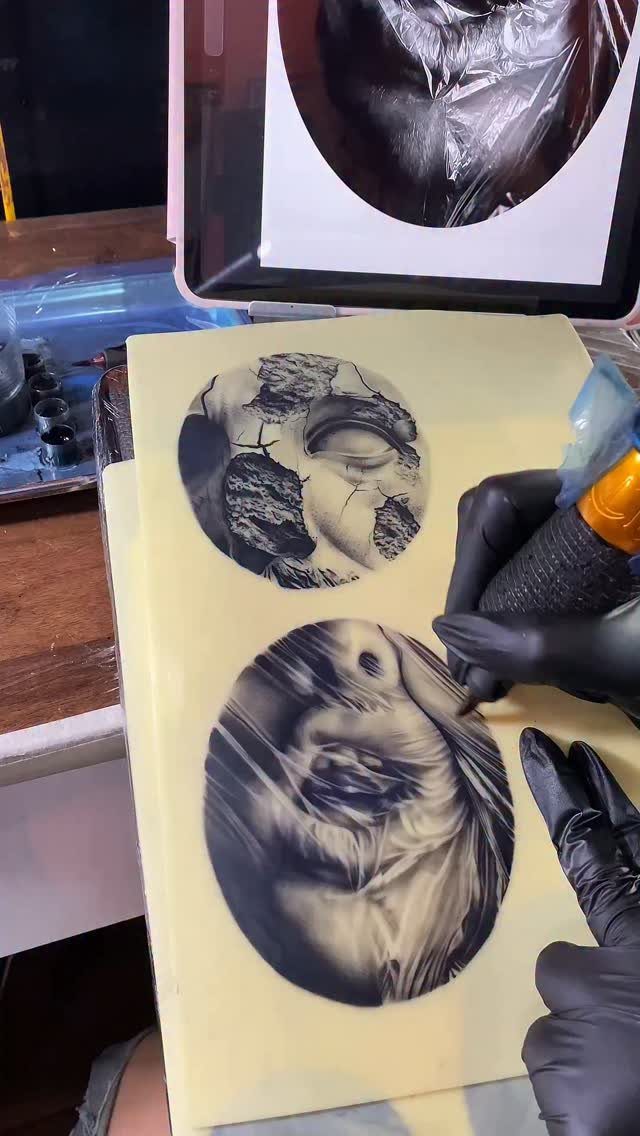 Tattoo artist in black gloves working on designs on a fake skin pad.