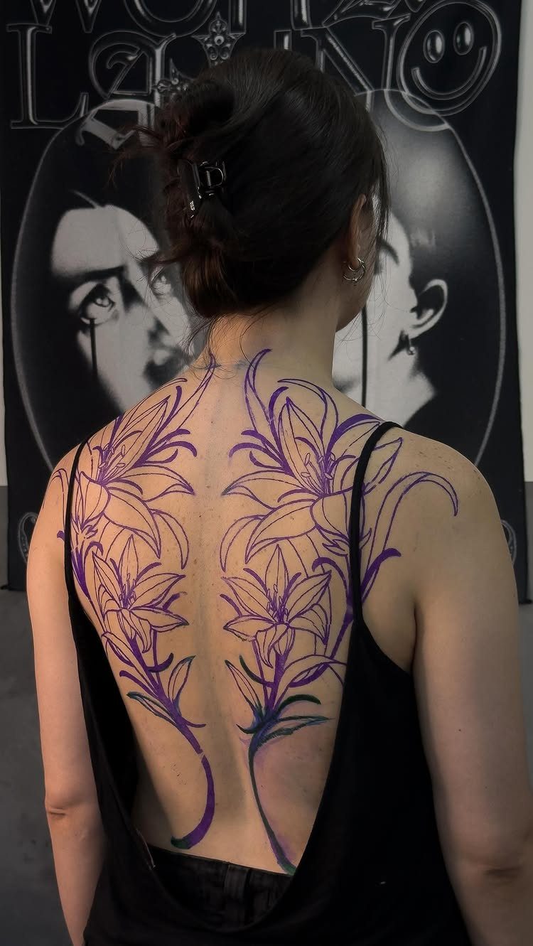 Woman's back with purple lily tattoo stencils applied to her skin.