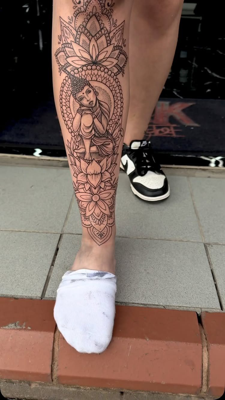 Detailed Buddha and lotus flower tattoo on a person's lower leg and ankle.