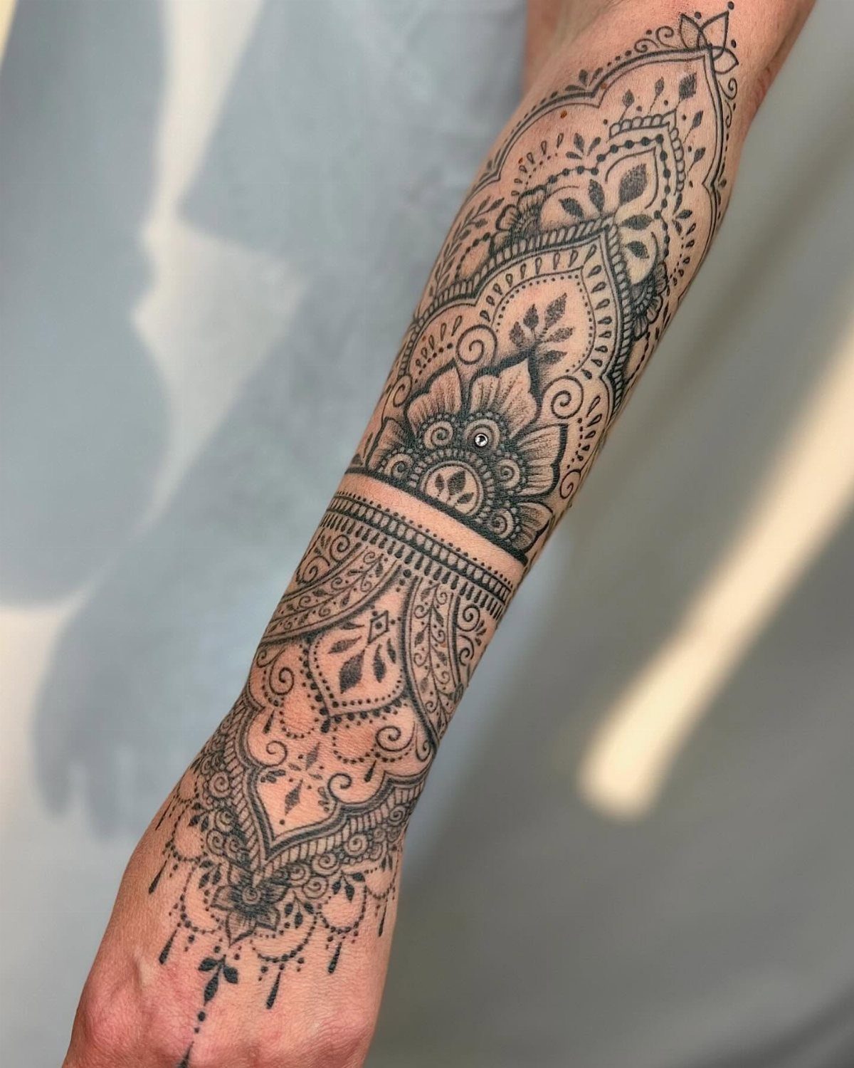 Intricate black ink mandala tattoo on a forearm resembling a traditional henna design