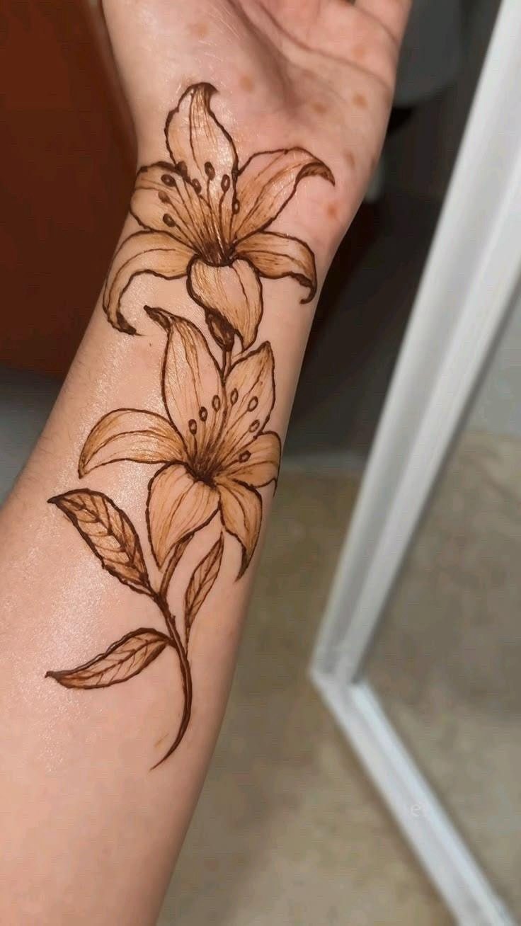 Brown henna lily flower design on a person's forearm and wrist.