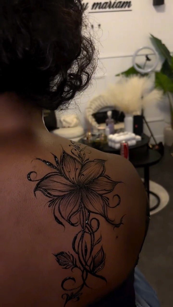 Black floral tattoo with swirling vines on a person's upper back.