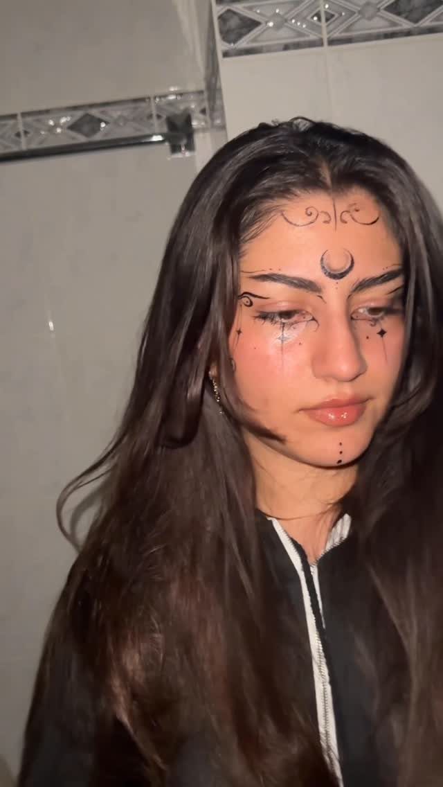 Woman with black henna-style tattoos on her forehead and chin posing indoors.