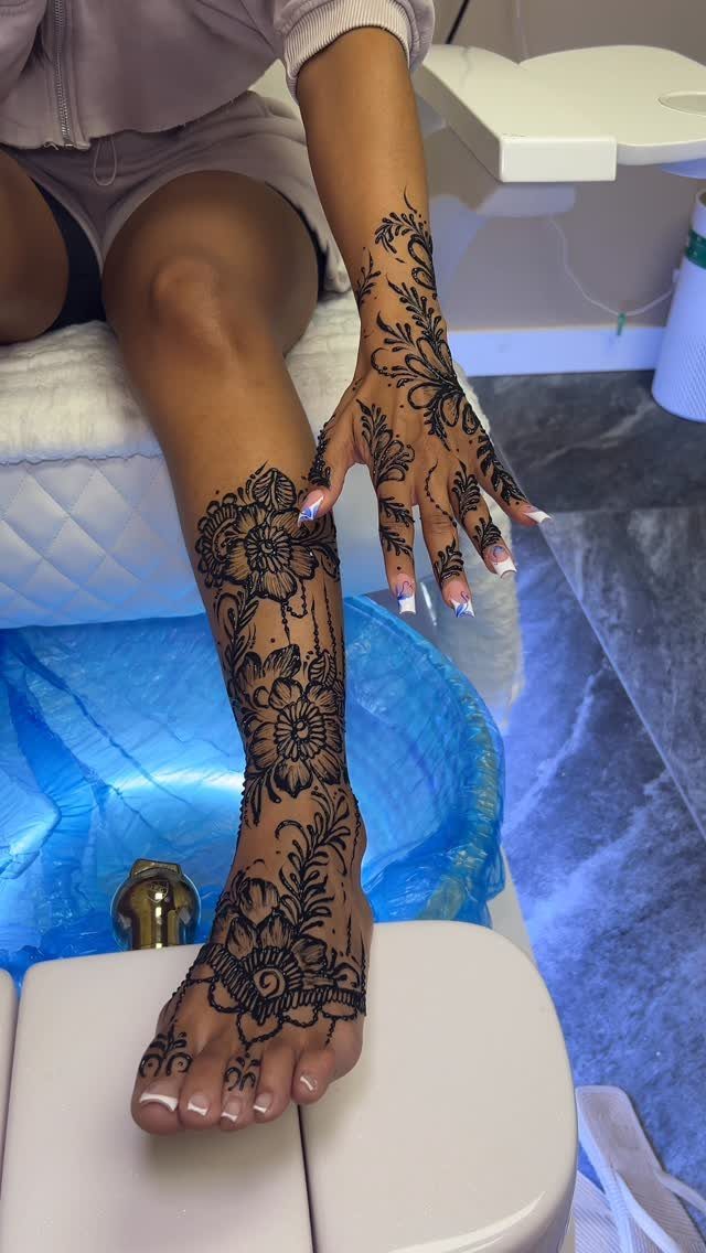 Foot and hand with intricate black henna-style floral tattoo designs in a salon.