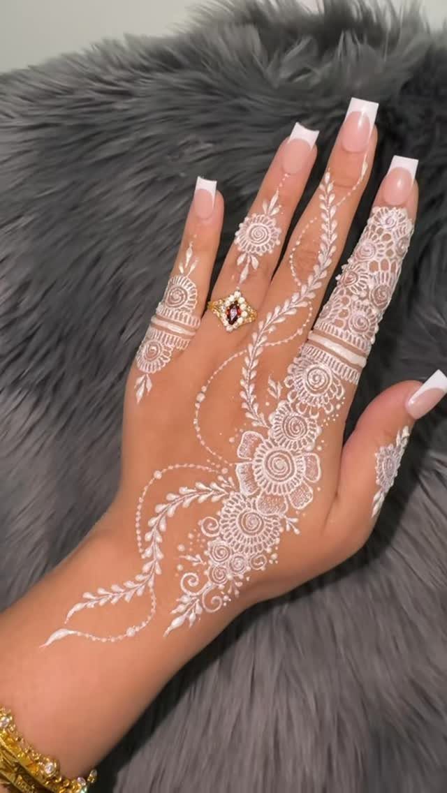 Hand with intricate white henna patterns and long white nails on grey fur.