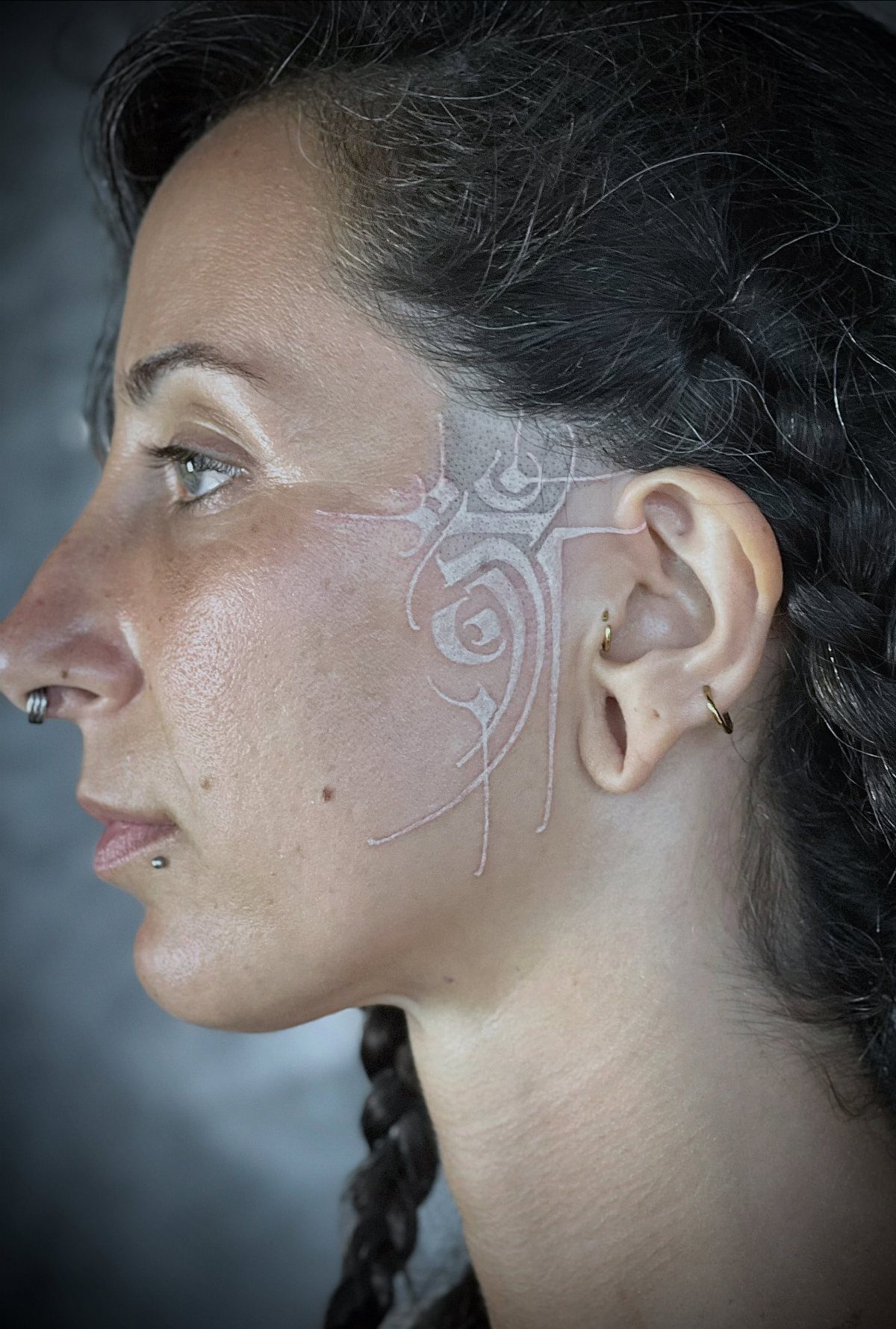 Woman with a white ink tattoo on her cheek and near her ear.