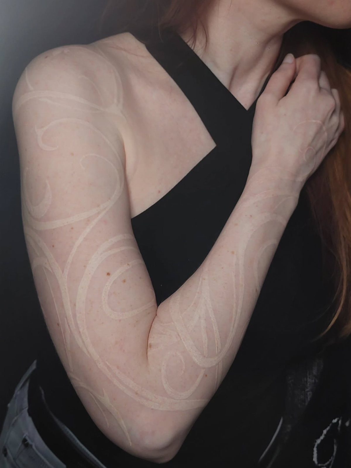 White ink tattoo with delicate swirling patterns on a person's arm and shoulder.