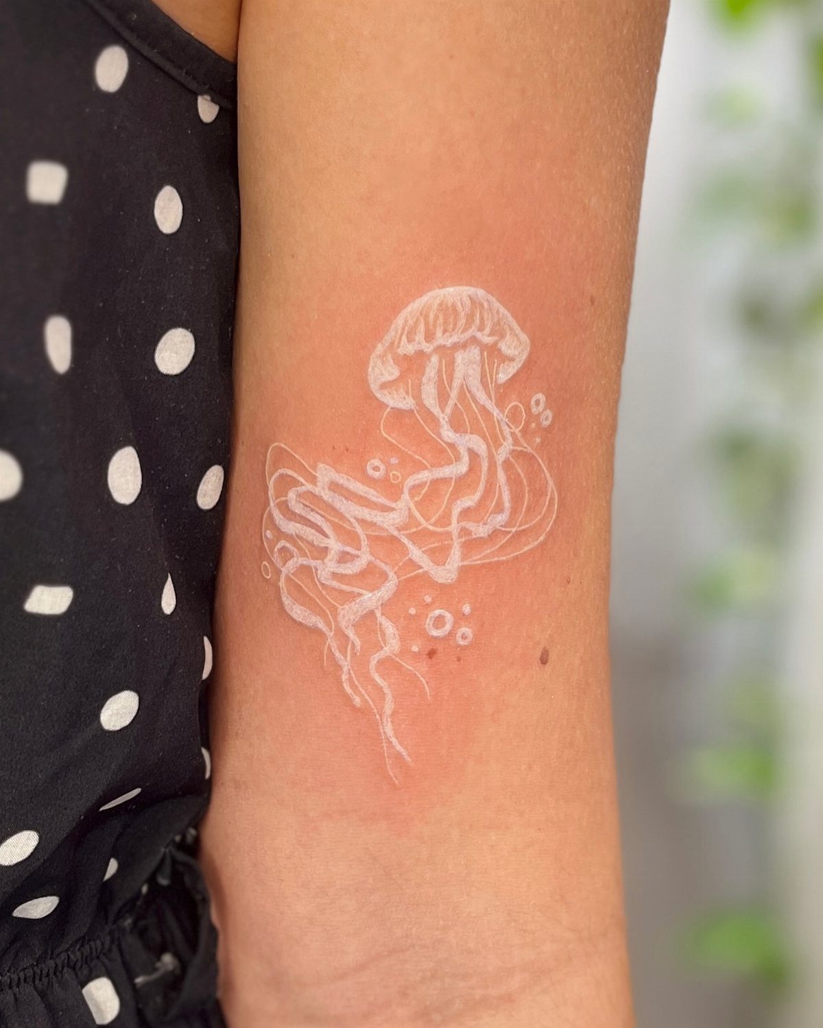 White ink jellyfish tattoo with flowing tentacles on a person's forearm
