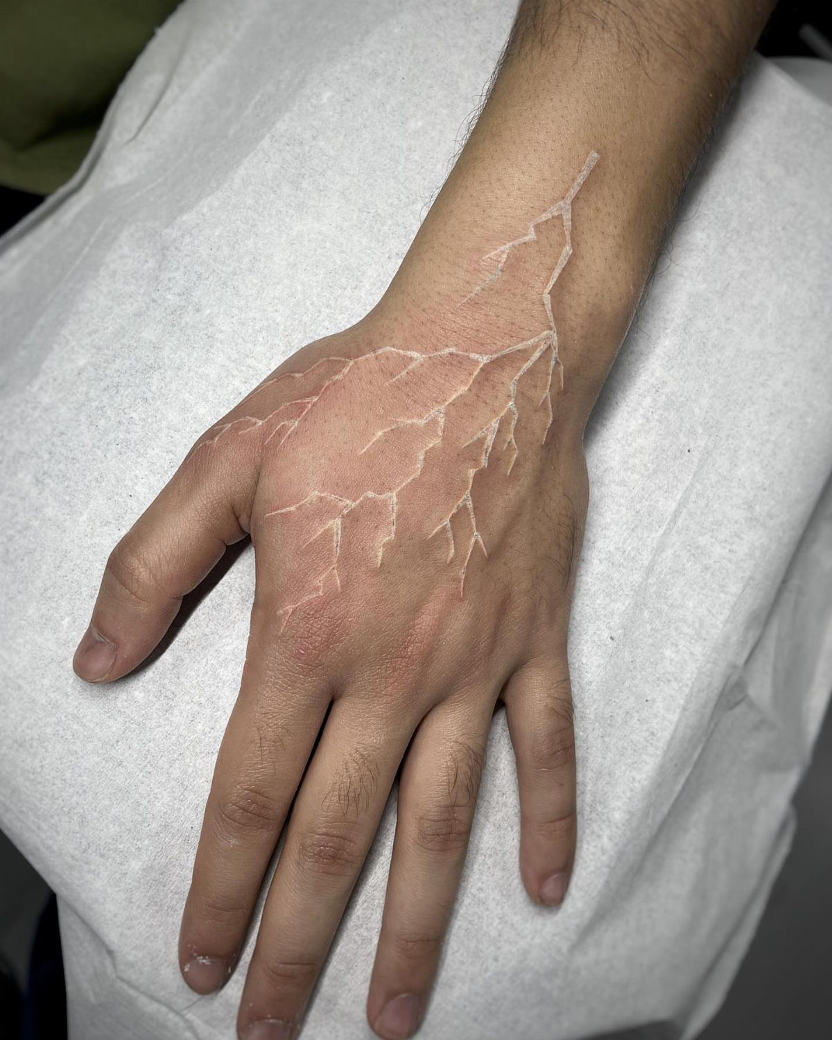 White ink lightning bolt tattoo on the back of a person's hand