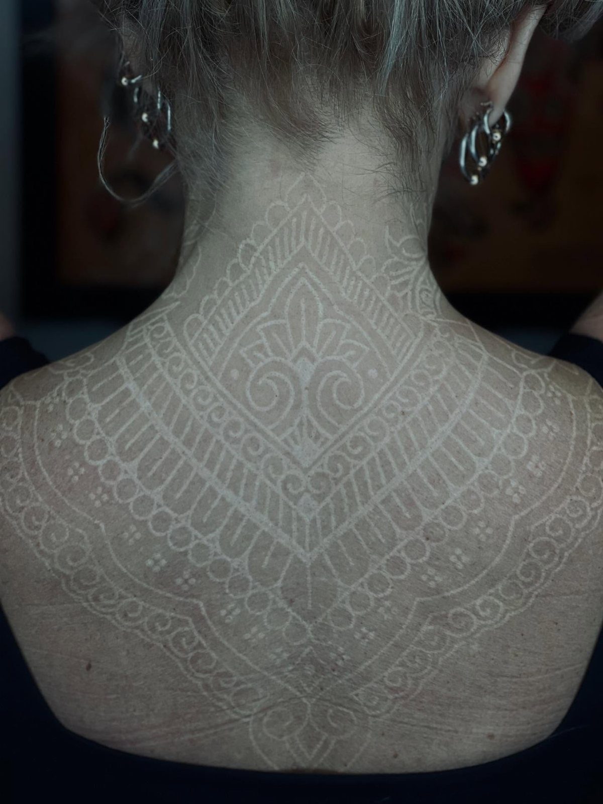 Intricate white ink mandala tattoo covering the upper back and neck of a person