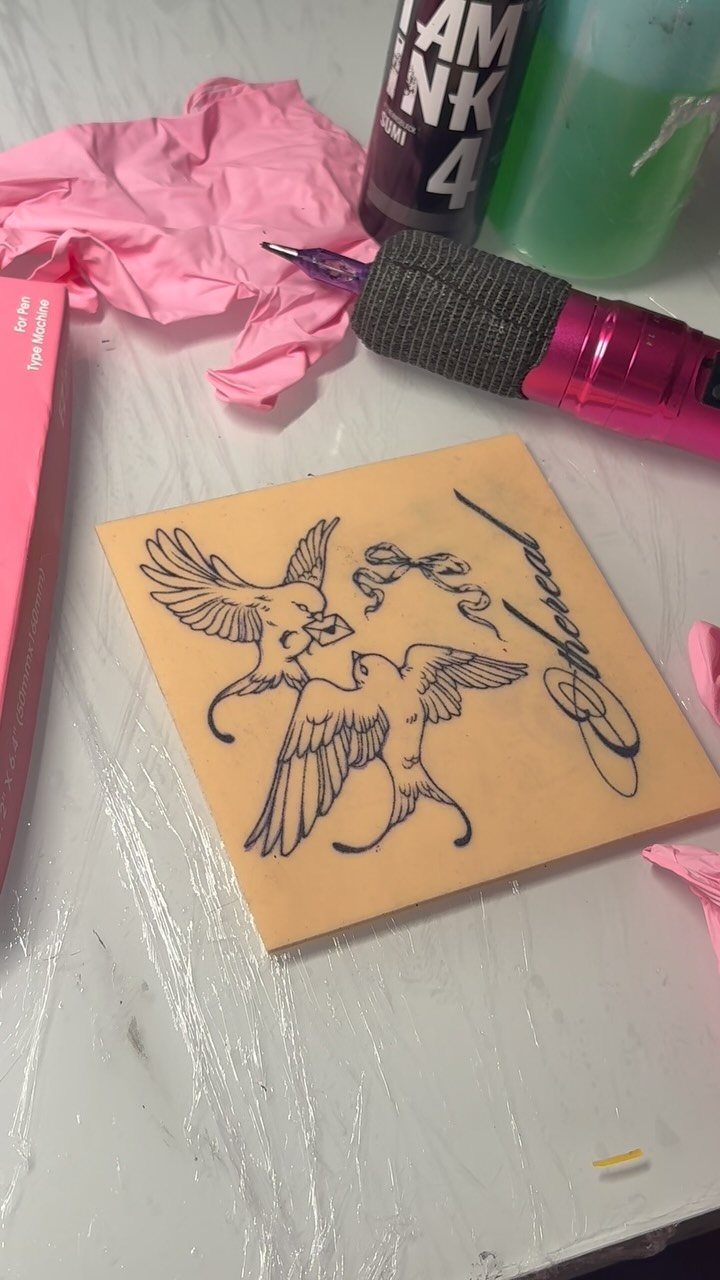 Tattoo of two birds on a square of tan fake skin with equipment.