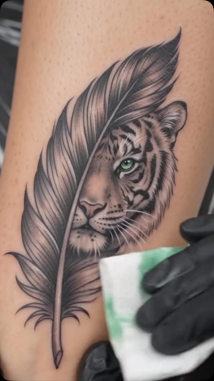 Tiger face tattoo partially covered by a feather on human skin