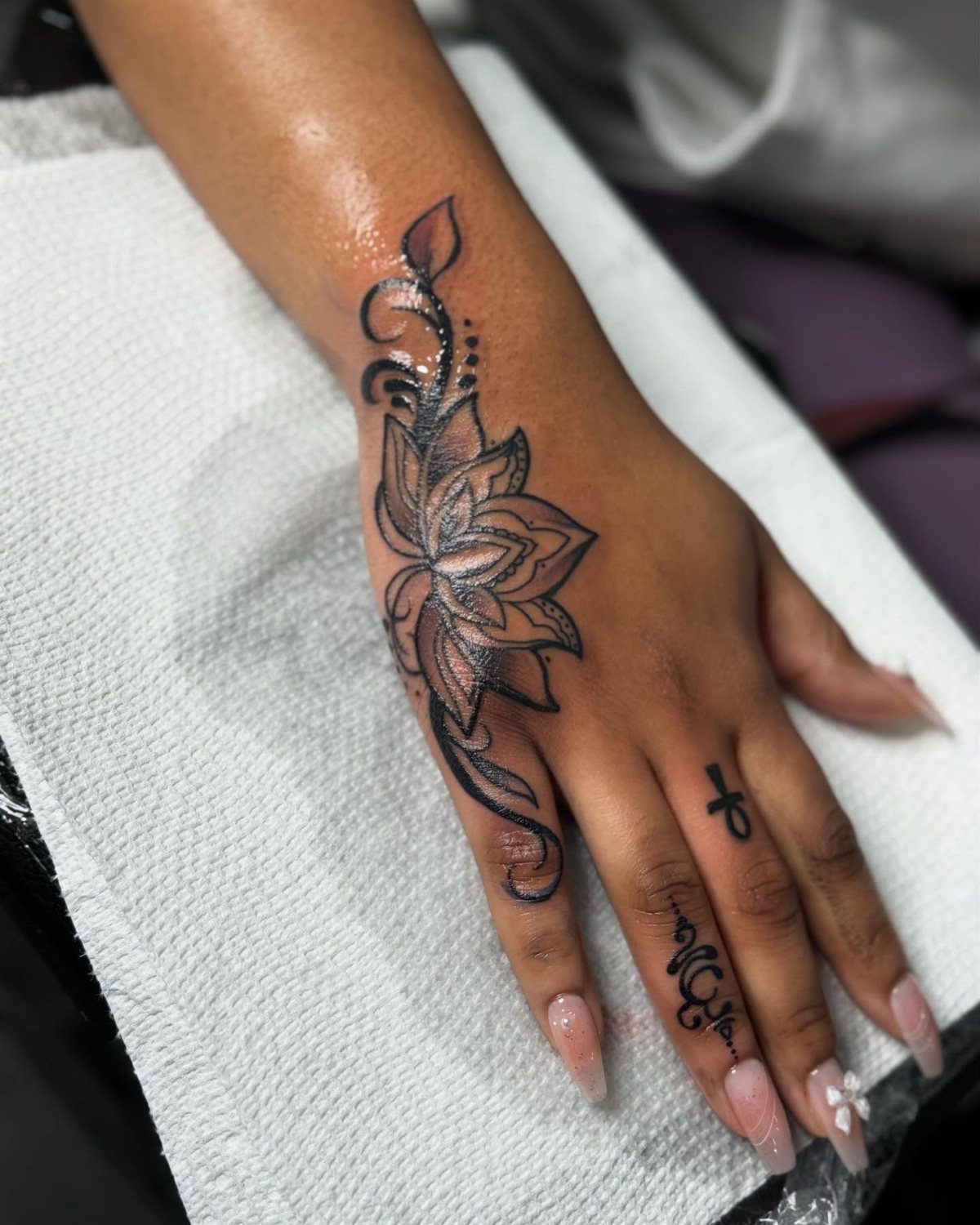Black ink flower tattoo with swirling vines on the back of a dark-skinned hand.