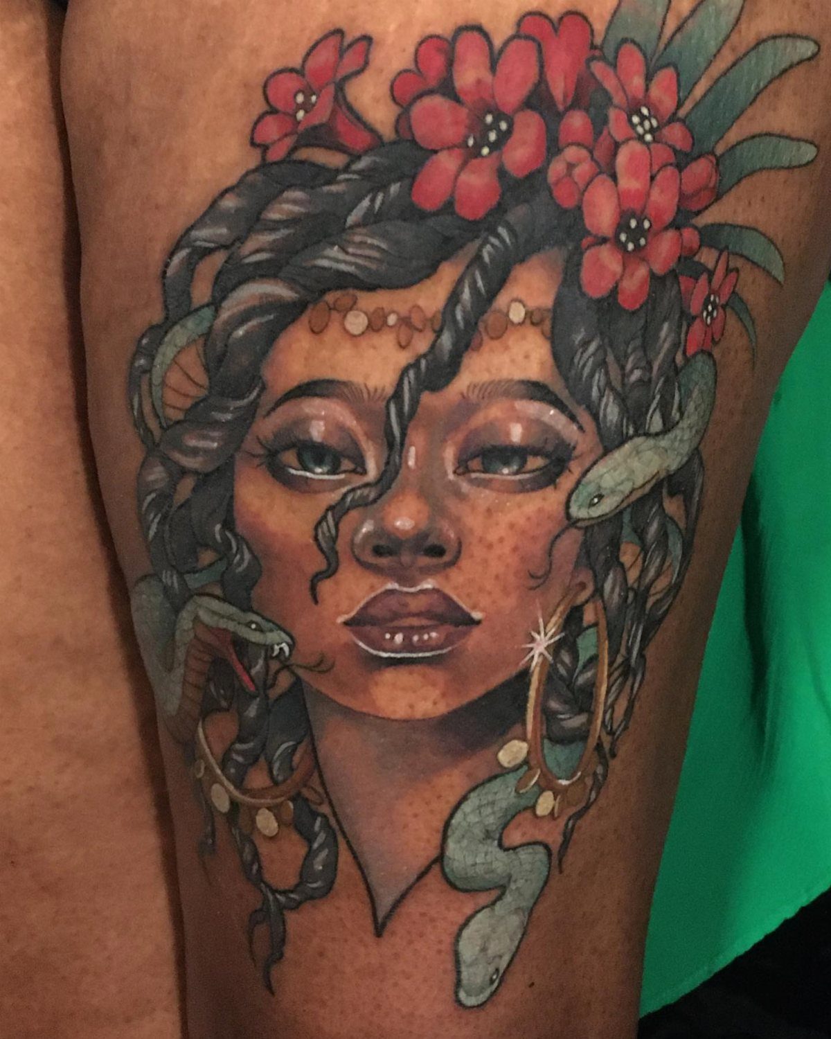 Color tattoo of a woman with dreadlocks, red flowers, and snakes on dark skin.