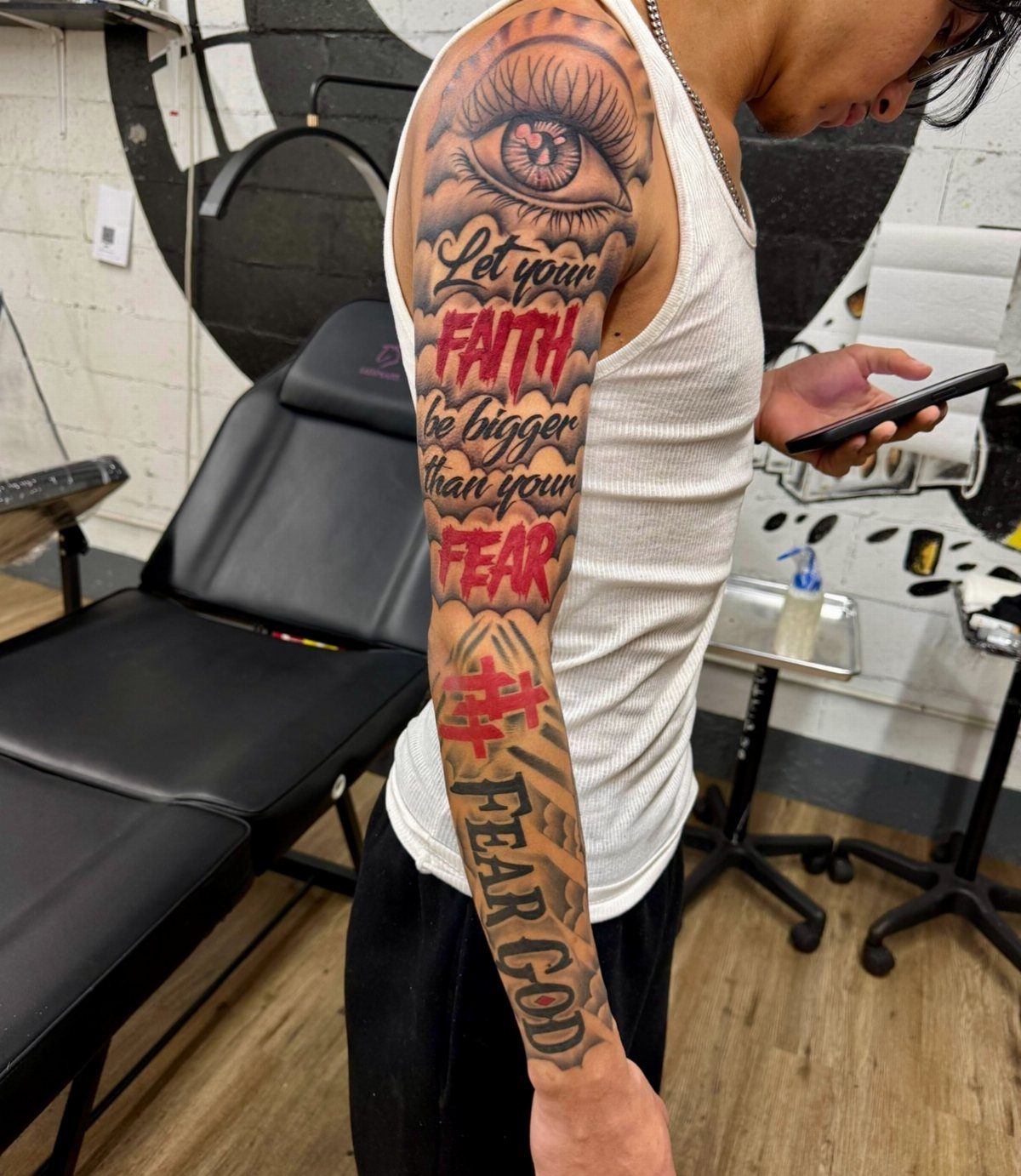 Tattooed arm with an eye and red script text on dark skin.
