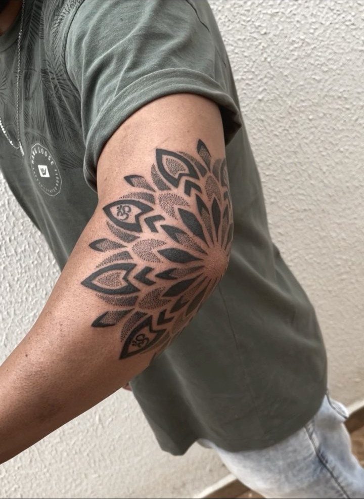 Mandala tattoo with symmetrical patterns on the upper arm of a dark-skinned person.