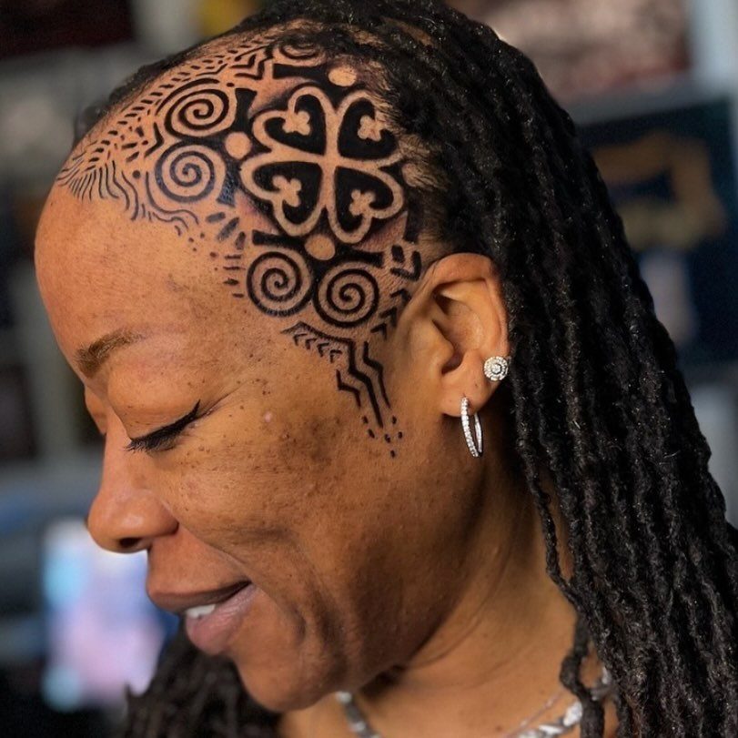 Black woman with a bold black tribal tattoo on her shaved temple.