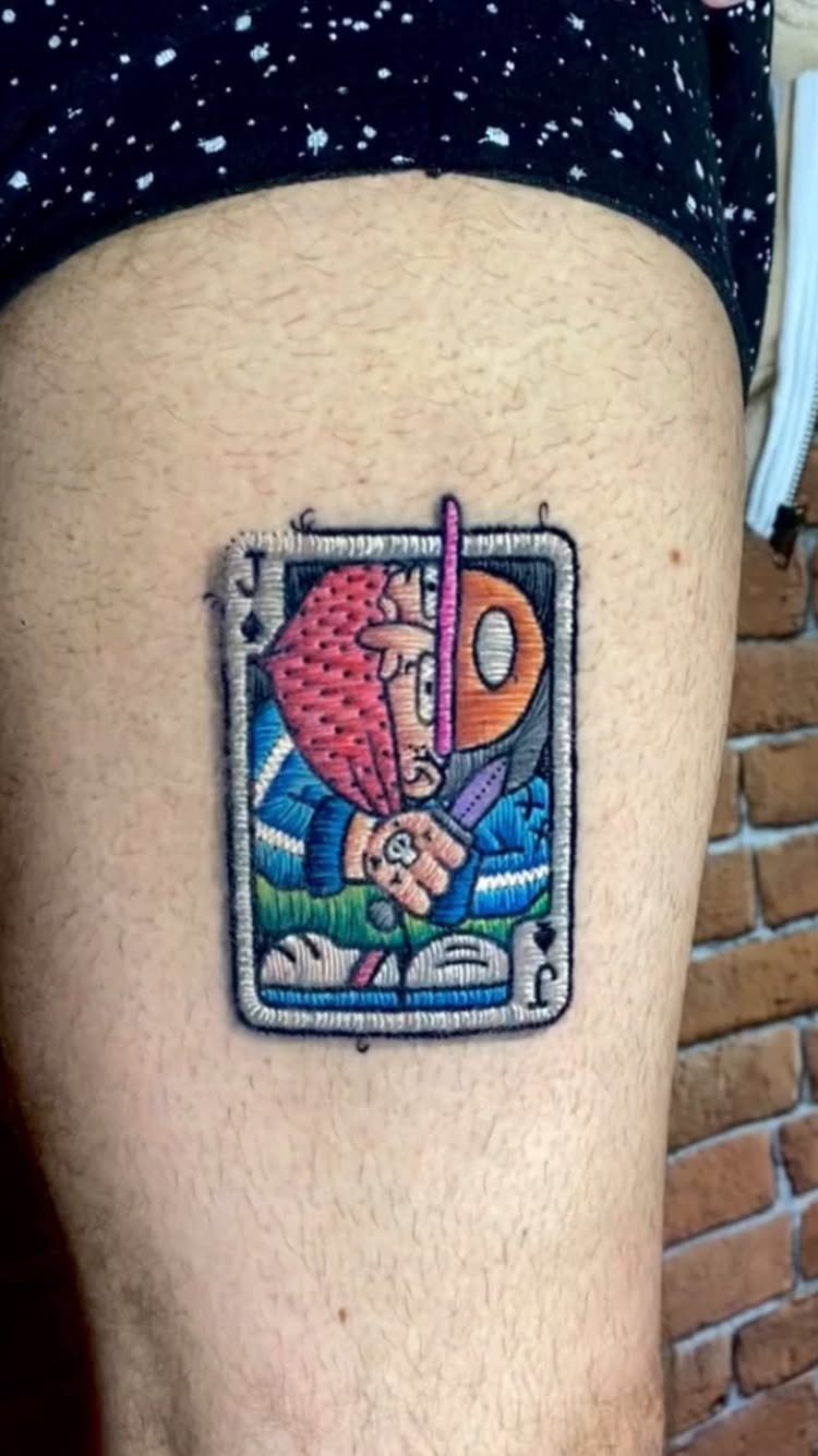 Cartoon character playing card tattoo with a thick white sticker-style border on skin
