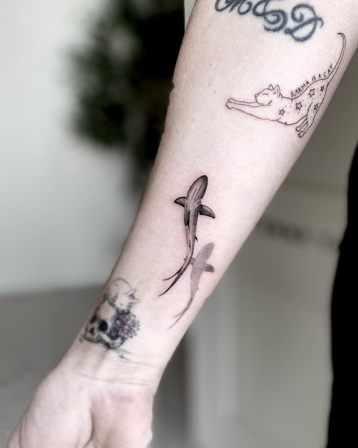 Shark tattoo on a forearm with a grey drop shadow creating a sticker effect.