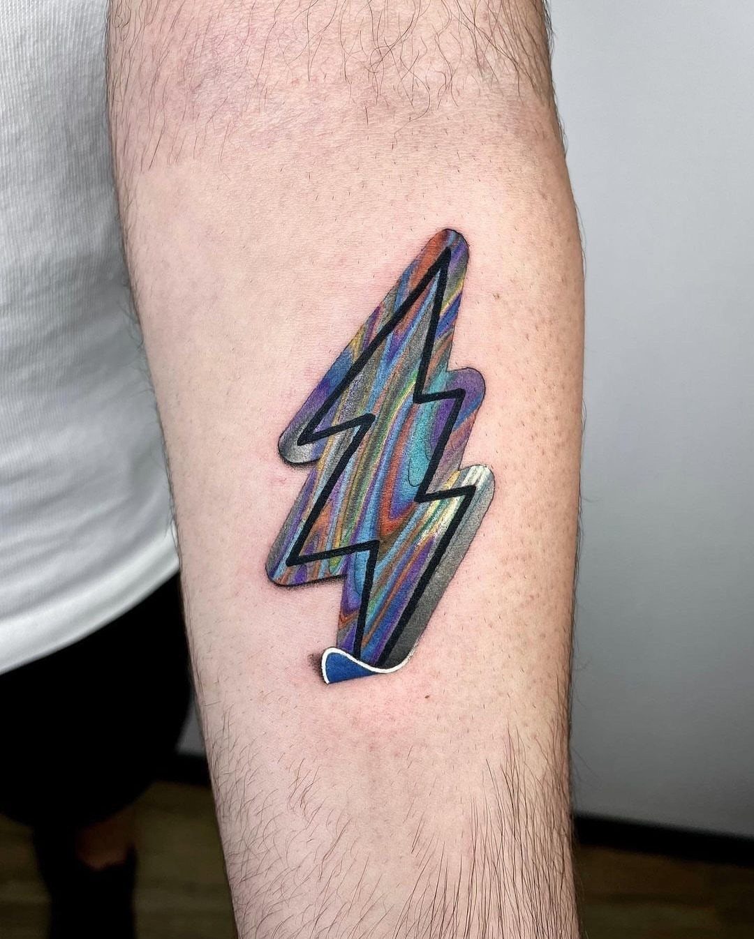 Holographic lightning bolt tattoo with a white border and shadow on a forearm