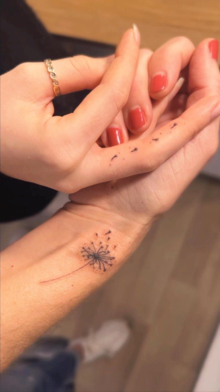 Dandelion seed head tattoo on a wrist with a hand resting above it.