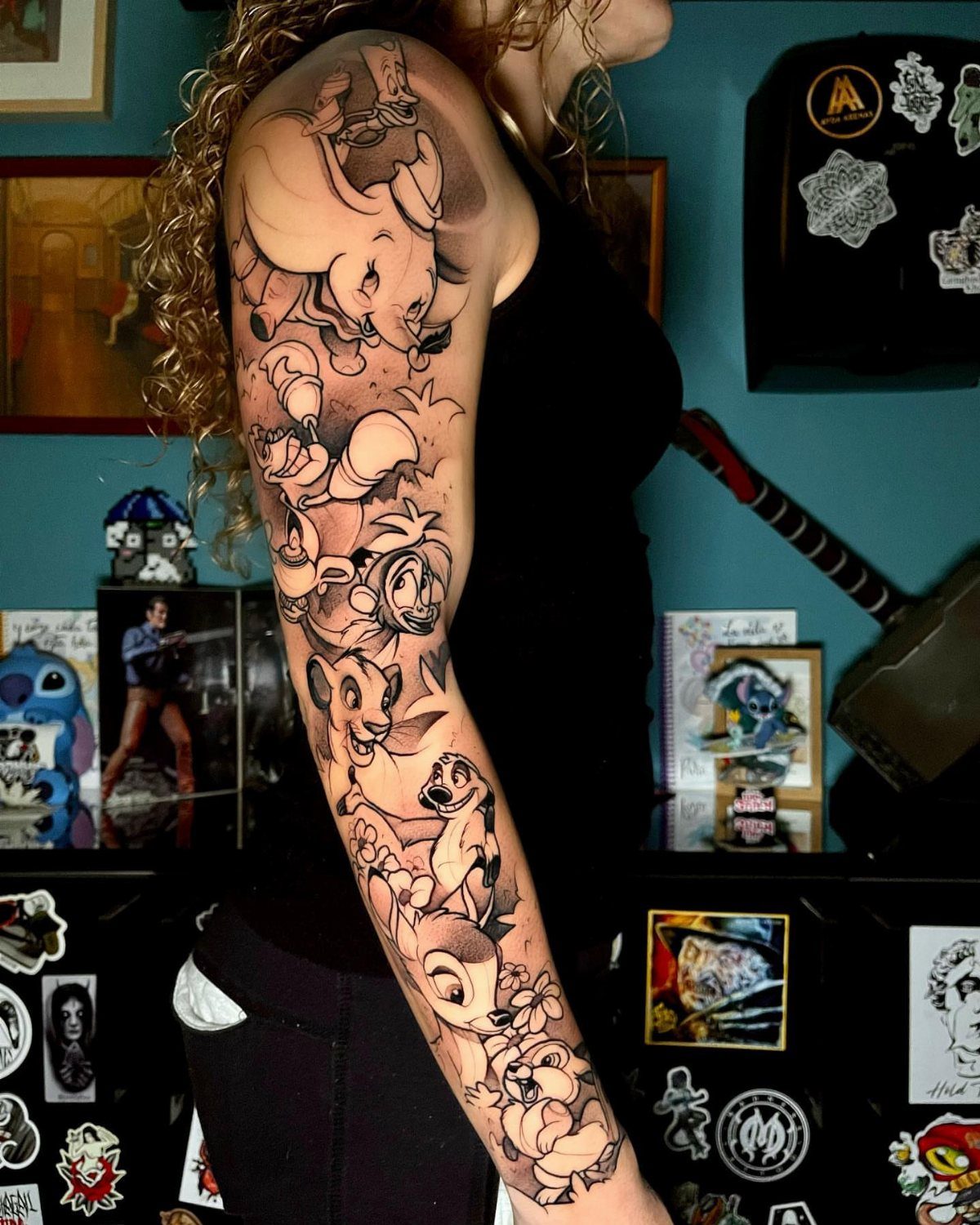 Full sleeve tattoo of Disney characters on a person's arm in black and grey.
