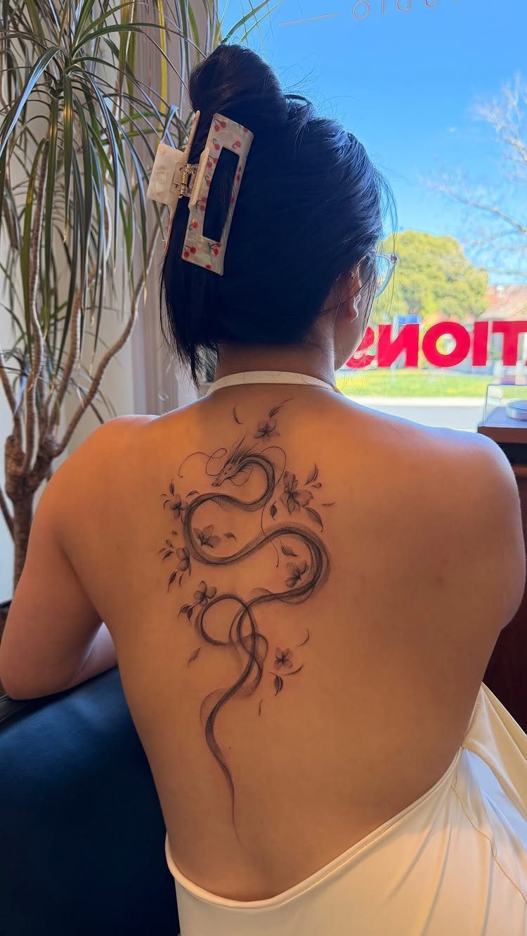 Slender black ink dragon tattoo with flowers on a woman's back