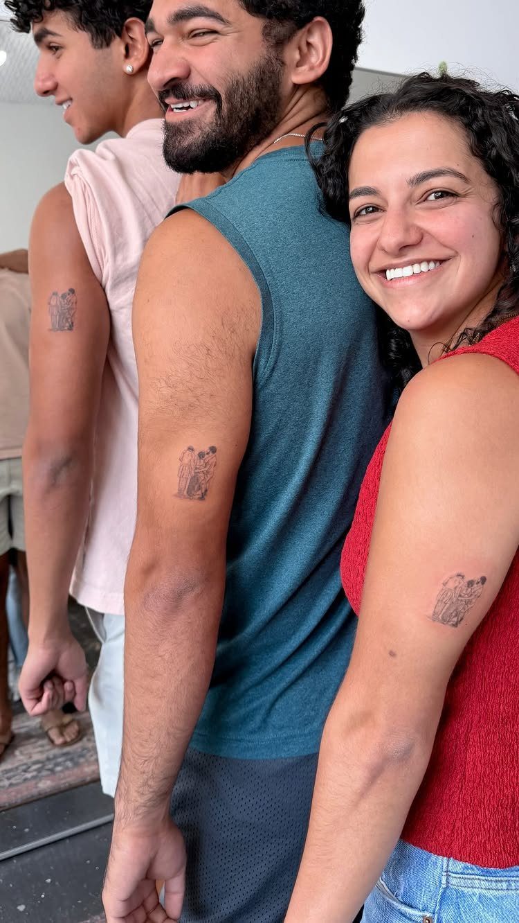 Three smiling people showing matching small tattoos on their upper arms.
