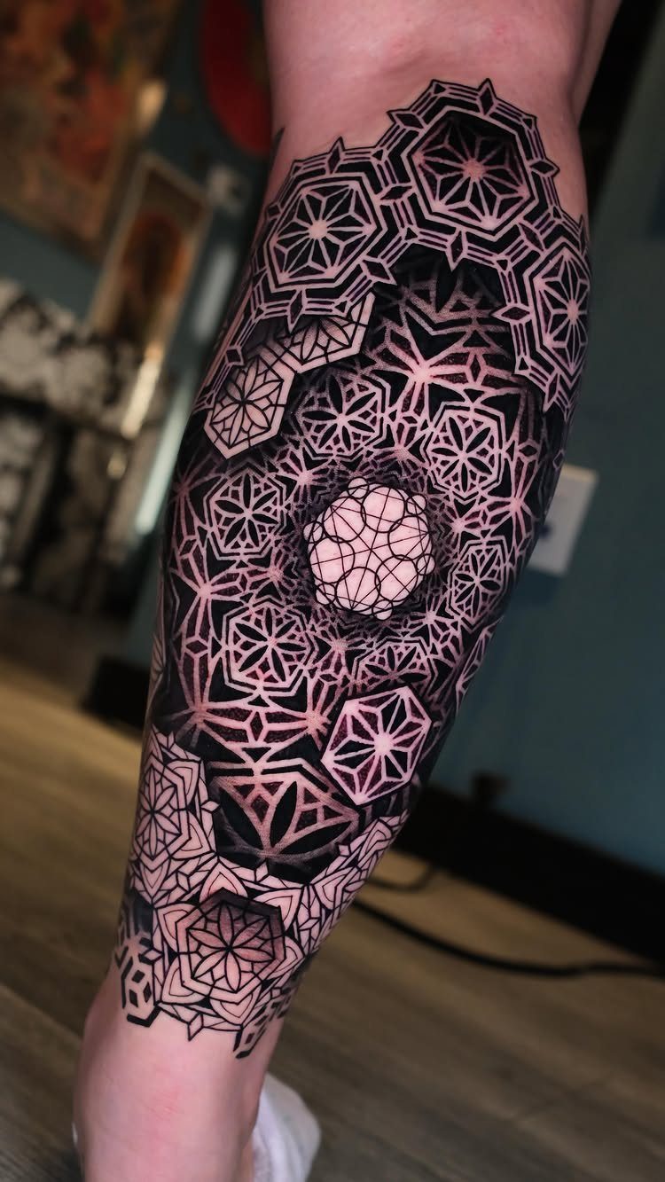 Intricate geometric black ink tattoo with symmetrical patterns on a person's lower leg.
