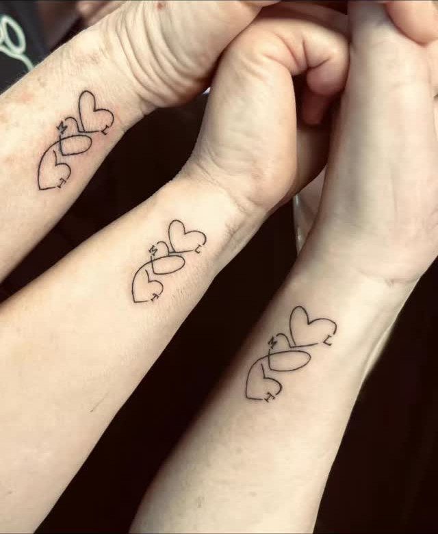 Three wrists with matching black ink interlocking heart tattoos on the inner wrist.