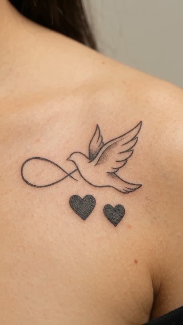 Bird and infinity symbol tattoo with two small hearts on a shoulder