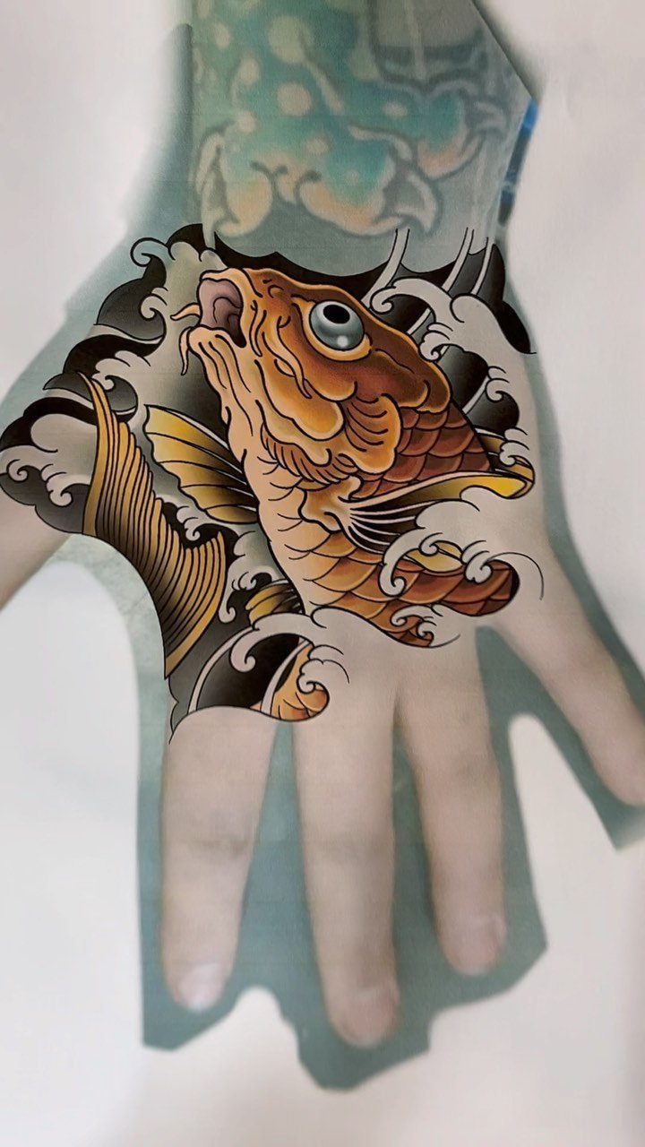 Orange koi fish tattoo with black waves on the back of a hand