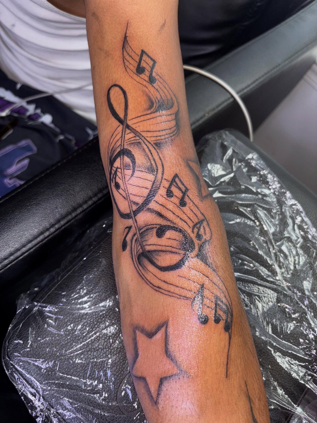 Treble clef and musical notes tattoo on a person's forearm with a star.