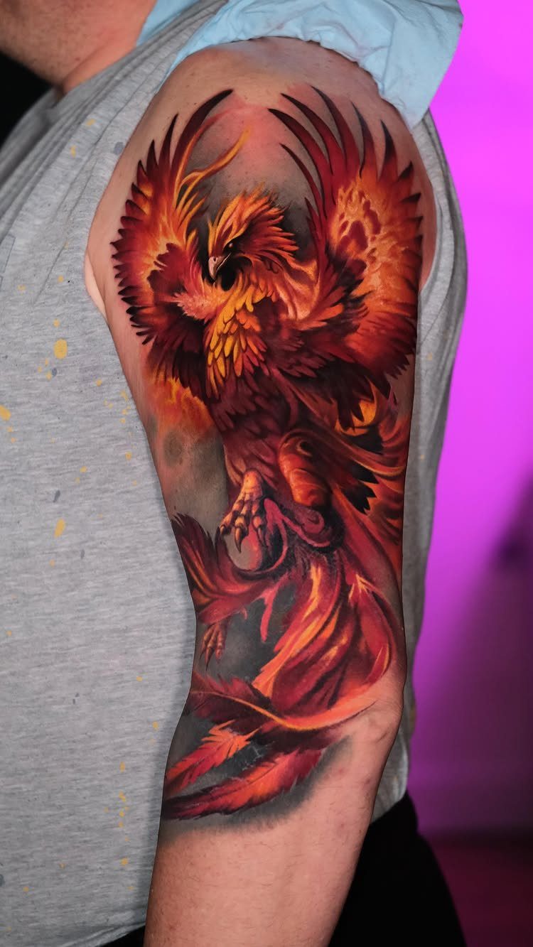 Phoenix tattoo on an upper arm featuring vibrant red and orange fiery feathers.
