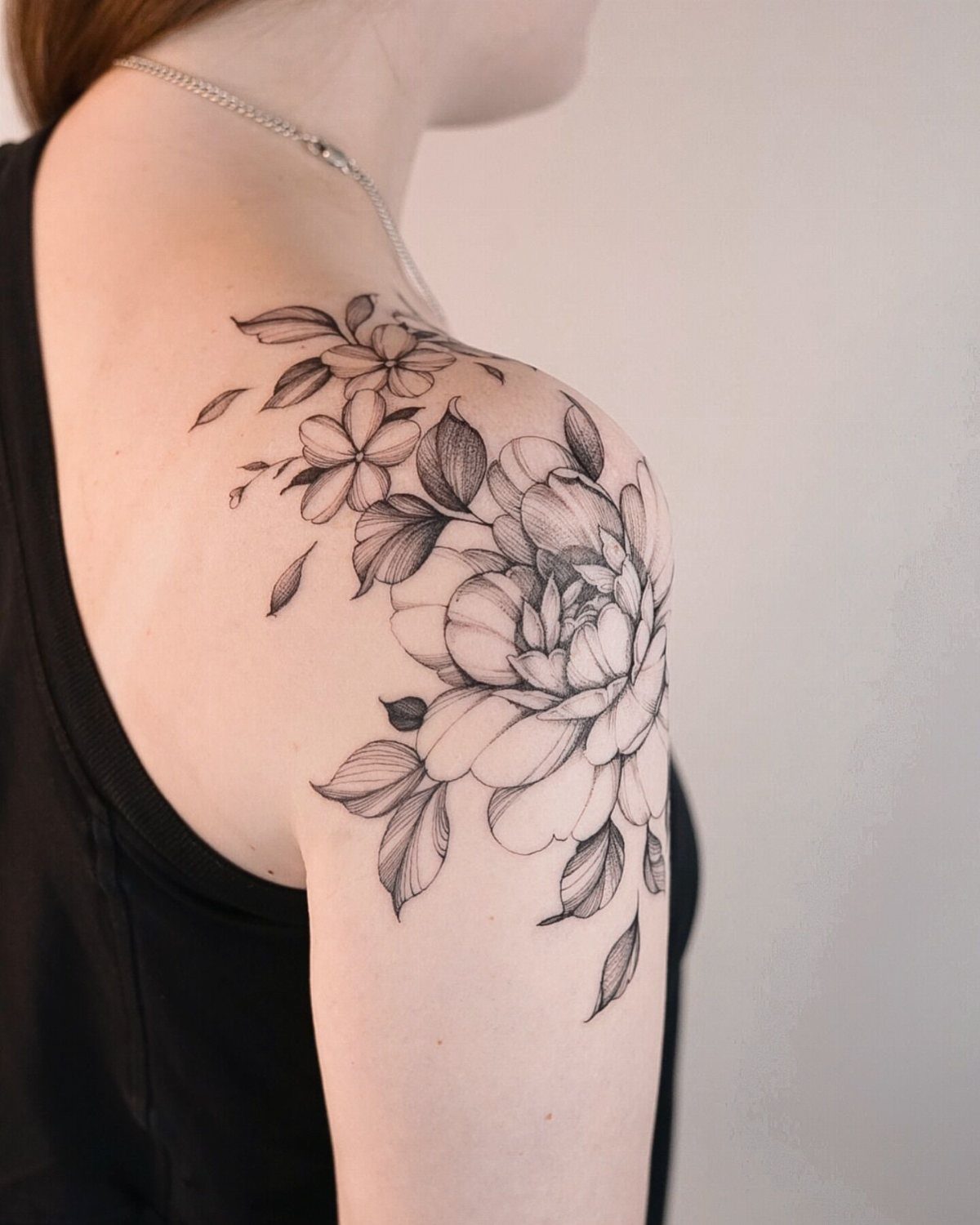 Floral tattoo with a large bloom and leaves on a person's shoulder.